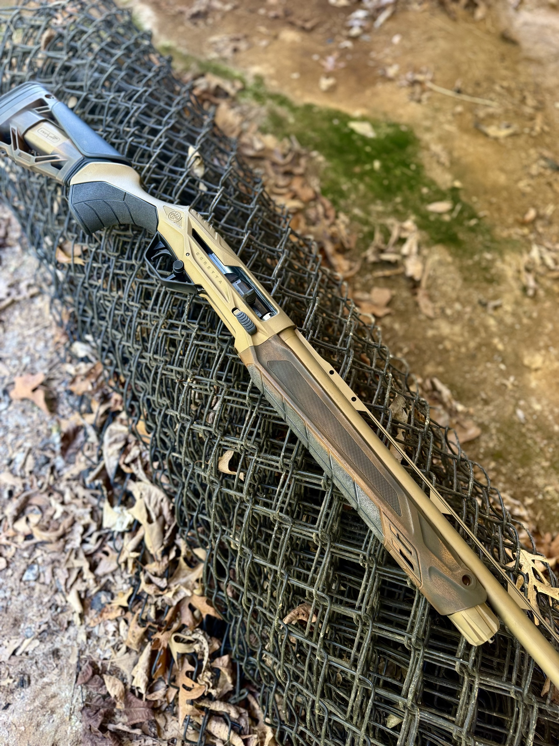 The chapter gun laid across a roll of wire fence, showing the custom dip from stock to barrel.